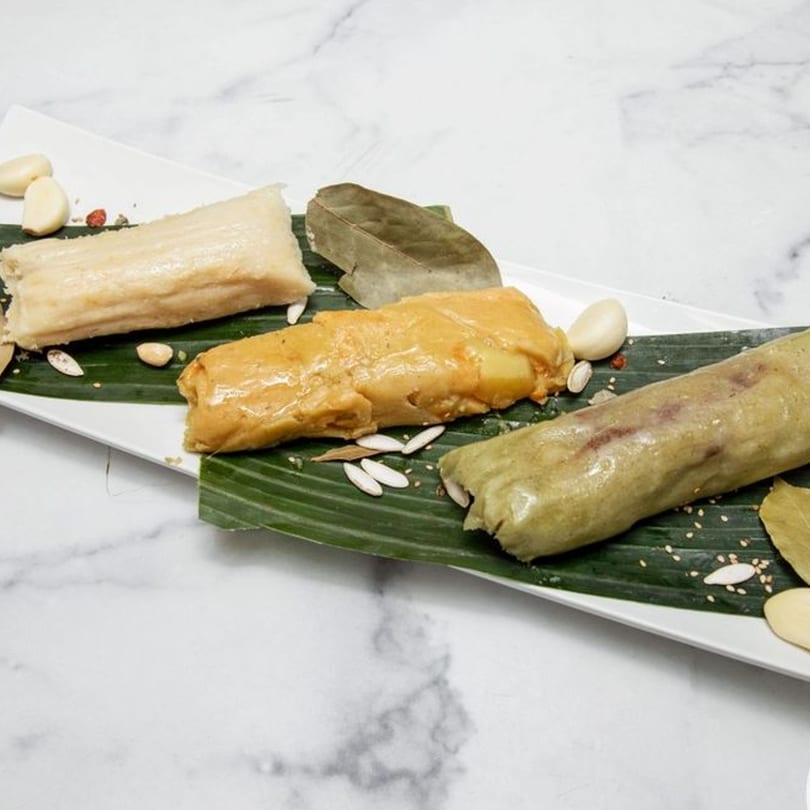 Three different colored halal tamales on banana leaves, garnished with garlic and seeds.