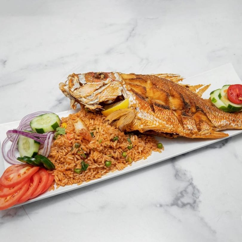 Whole fried fish with lemon, red rice, peas, and a side salad of tomatoes, cucumbers, and red onions.