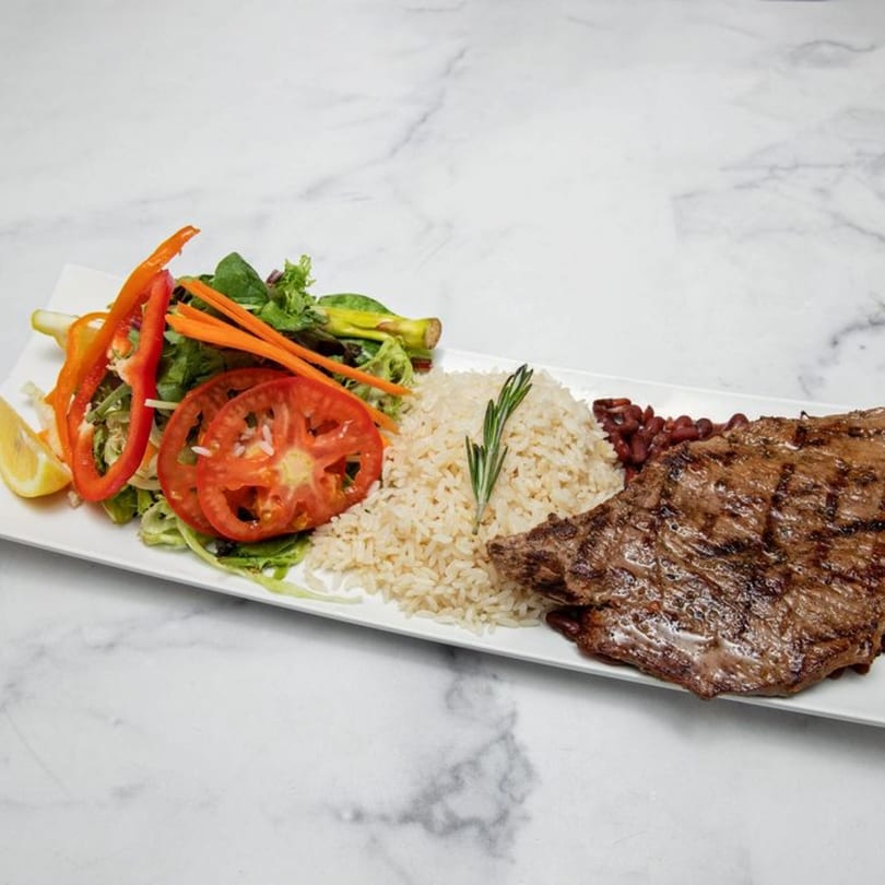 Grilled steak with rice, red beans, and a fresh salad with tomatoes and bell peppers.