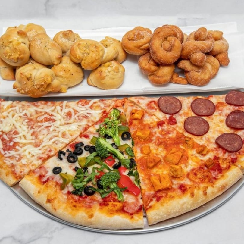 A large pizza with four different toppings, garlic knots, and cinnamon knots on a white surface.