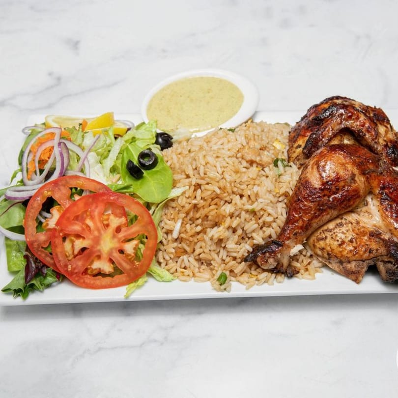 Halal roasted chicken with rice, a side salad, and a small bowl of green sauce.