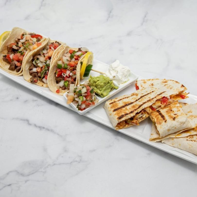 A platter of La Estacion tacos and quesadillas with guacamole, salsa, and sour cream.